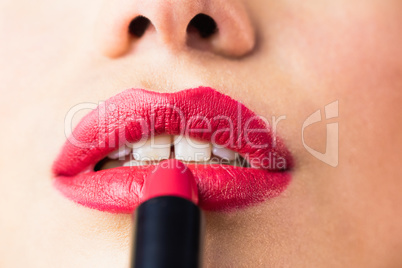 Beautiful woman applying red lipstick on lips against black background