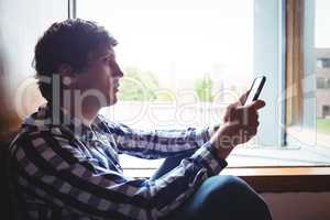 Student using mobile phone near window