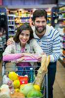 Happy couple leaning on trolley at supermarket
