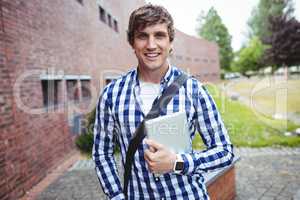 Smiling student standing in campus with digital tablet