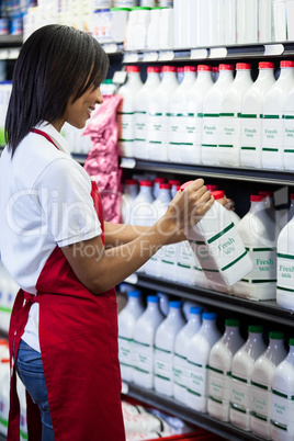 Female staff arranging milk bottle in shelf