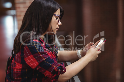 Female student using mobile phone in corridor