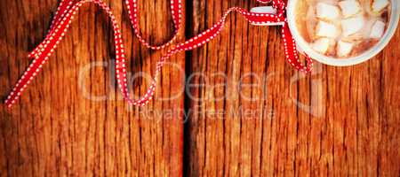 Cup of coffee with sugar cube tied with red ribbon on wooden plank