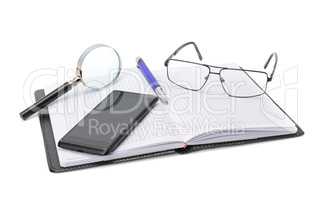 Notebook, glasses, cell phone and magnifying glass