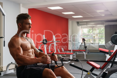 At gym. Sexy shirtless guy exercising on simulator