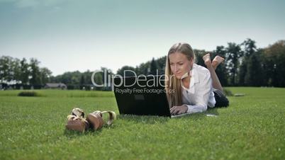 Businesswoman lying on green grass with laptop