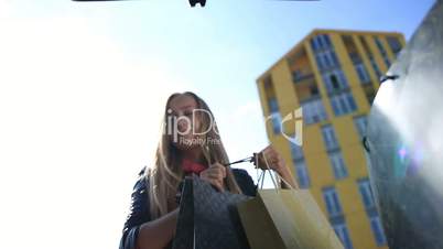 Smiling woman putting shopping bags into car trunk