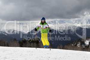 Young skier jump with ski poles in sun mountains and cloudy gray