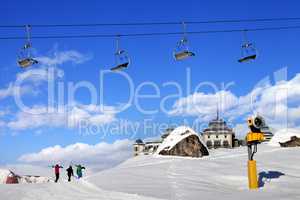 Chair-lift in blue sky and three skiers on ski slope at sun nice