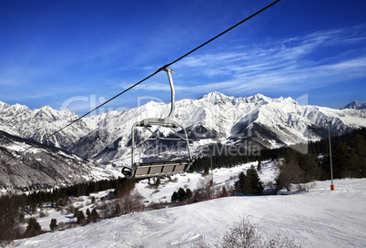 Ski slope and chair-lift in snow winter mountains at sun windy d