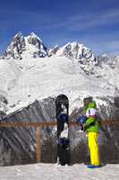 Young snowboarder with helmet in hands and snowboard on viewpoin