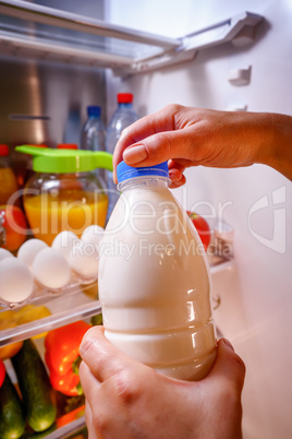 Woman takes the milk from the open refrigerator