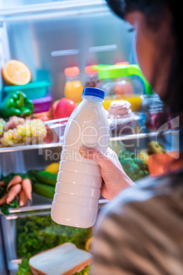 Woman takes the milk from the open refrigerator