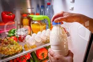 Woman takes the milk from the open refrigerator