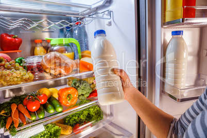 Woman takes the milk from the open refrigerator