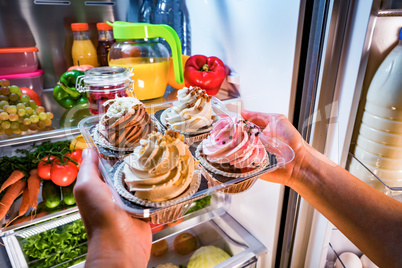 Woman takes the sweet cake from the open refrigerator