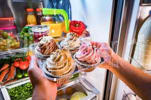 Woman takes the sweet cake from the open refrigerator