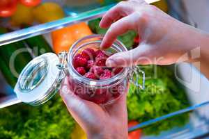Woman takes the fresh raspberries from the open refrigerator