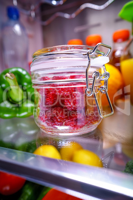 Fresh raspberries in a glass jar on a shelf open refrigerator