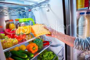 Woman takes the piece of cheese from the open refrigerator