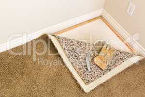 Gloves and Utility Knife On Pulled Back Carpet and Pad In Room.