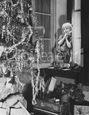 Young boy admiring Christmas tree and presents from window