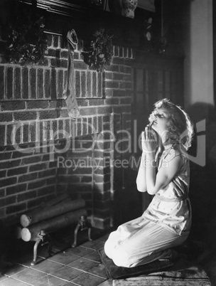 Portrait of teenage girl praying at hearth with Christmas stocking