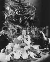 Teenage girl hugging stuffed animals under Christmas tree