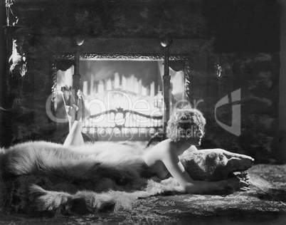 Woman relaxing on bear rug in front of fire