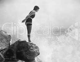 Female swimmer on rock above crashing surf
