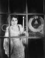 Woman with candle and Christmas wreath in window