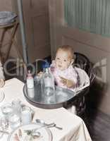 Baby in highchair with large and small bottles