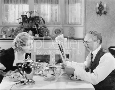 Couple reading newspaper at breakfast table