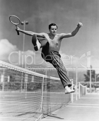 Male tennis player jumping over net