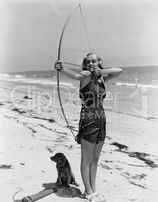 Woman shooting bow and arrow on beach