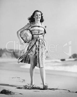 Woman walking on beach carrying ball