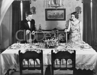 Couple lighting candles on table set for dinner