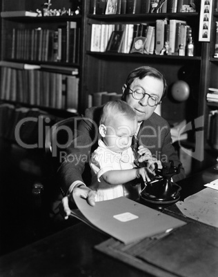 Father helping baby use telephone