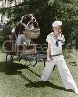 Girl in sailor suit pulling dog in basket