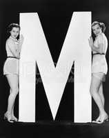 Two women posing with huge letter M