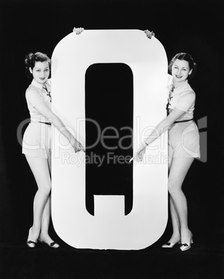 Two women pointing at huge letter Q