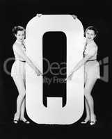 Two women pointing at huge letter Q