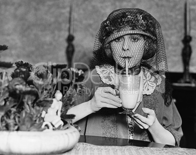 Veiled woman drinking beverage