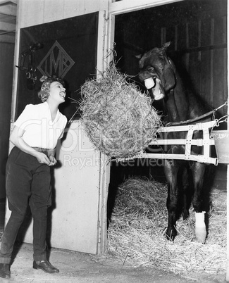 Woman pretending to eat hay bale with horse