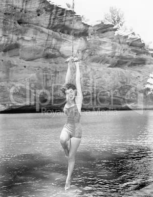 Woman hanging from rope swing over water