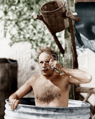 Man sitting in a barrel taking a bath and looking through his monocle