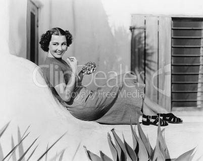 Young woman sitting on a terrace smiling and eating grapes