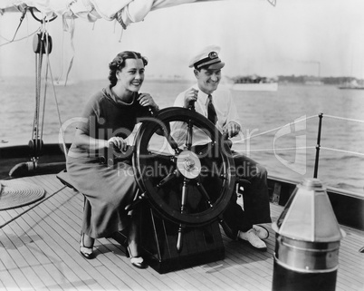 Couple sitting on the deck of a sailboat steering the boat