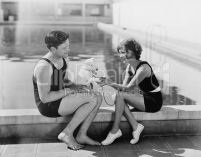 Couple sitting with their puppy next to a pool