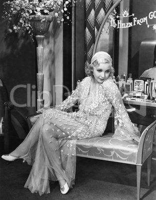 Young woman in an evening gown sitting on an upholstered bench